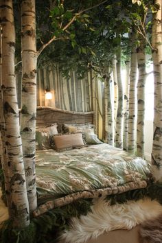 a bed in the middle of some trees with blankets on it and pillows under them