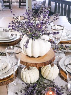 the table is set with white pumpkins, lavender and glassware for dinner guests