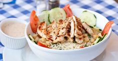 a white bowl filled with chicken and veggies on top of a blue and white checkered table cloth