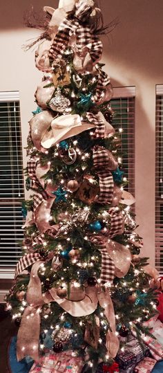 a decorated christmas tree in the corner of a living room with plaid and bows on it