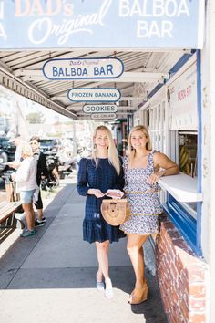 two women are standing in front of a bar and some people on the sidewalk behind them