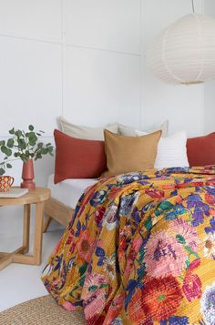 a bed with colorful bedspread and pillows in a white room next to a table