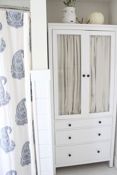 a white cabinet sitting in the corner of a room next to a shower curtain and toilet