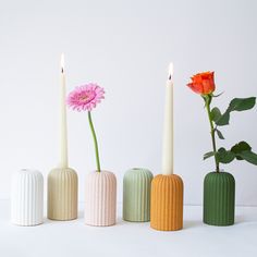 three vases with candles and flowers in them on a white surface, next to each other