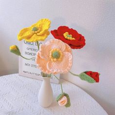 three crocheted flowers in a white vase on a table next to a sign