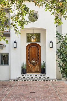 a large wooden door on the side of a white building with potted plants in front of it