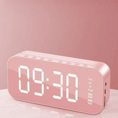 a pink alarm clock sitting on top of a white table next to a red wall