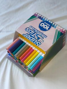 a box of colored pencils sitting on top of a bed