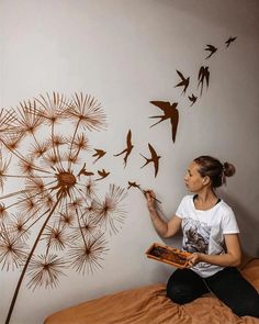 a woman sitting on top of a bed next to a dandelion wall decal