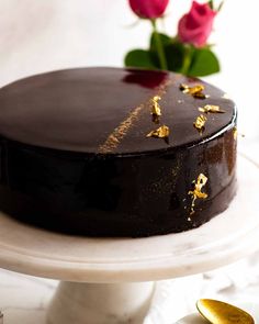 a chocolate cake sitting on top of a white plate next to a gold spoon and rose