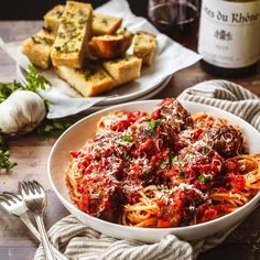 a bowl of spaghetti with meatballs and parmesan bread next to it on a wooden table