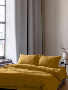 a bed with yellow sheets and pillows in front of a window