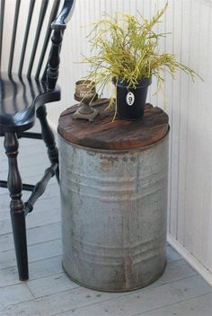 a potted plant sitting on top of a metal barrel next to a wooden chair