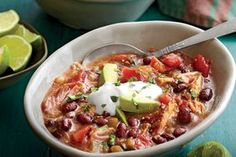 a white bowl filled with chili and beans next to limes on a blue table