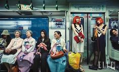 several people sitting on a subway car with their backs to each other, one woman holding a purse and the other standing up