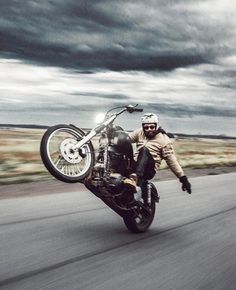 a man riding on the back of a motorcycle down a road under a cloudy sky