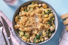 a bowl filled with pasta and vegetables on top of a blue table cloth next to silverware