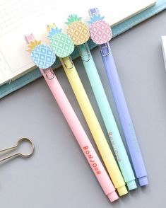 four different colored pens sitting on top of a desk next to a pair of scissors