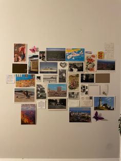 a white wall covered in pictures and postcards on it's side, with a vase filled with flowers