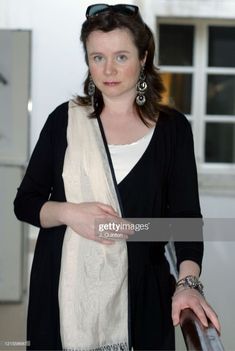 a woman in black jacket and white scarf standing next to an open door with her hand on