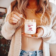 a woman holding a jar of food in her hands while wearing a sweater and jeans