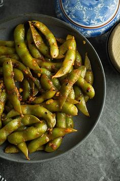 green beans in a bowl next to a blue and white vase on a table top