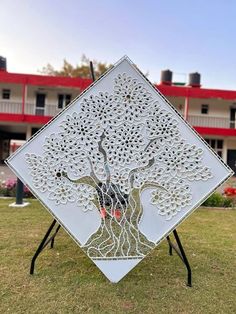 a metal sculpture with a tree on it in front of a red and white building