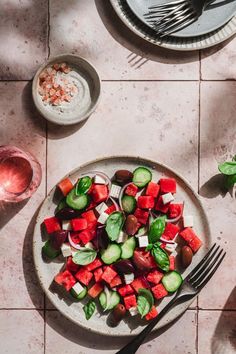 a white plate topped with cucumbers and red onions next to a bowl of tomatoes