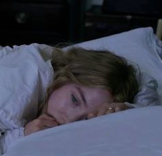 a woman laying in bed with her head on the pillow and looking at the camera