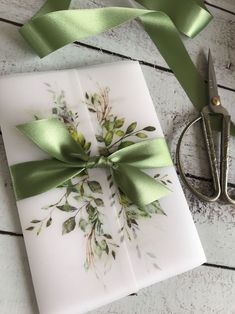 a gift wrapped in white paper with a green bow and ribbon on it next to scissors