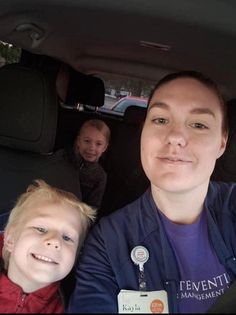 two children and an adult sitting in the back seat of a car, smiling at the camera