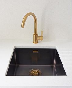 a kitchen sink with a gold faucet on the side and a white counter top