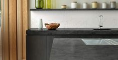 a modern kitchen with black counter tops and wooden shelves on the wall, along with white vases