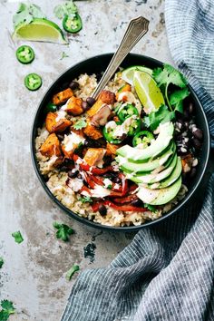 a bowl filled with rice, avocado and black beans next to sliced limes