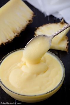 a spoon full of cream sitting on top of a black table next to sliced pineapples