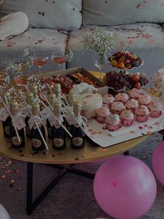 a table topped with lots of cupcakes and wine bottles next to pink balloons