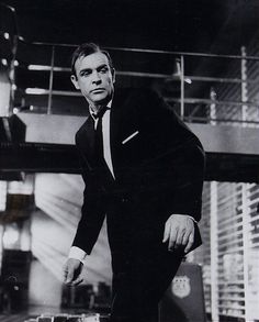 a black and white photo of a man in a suit leaning on a piece of luggage