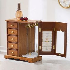 an open wooden jewelry box sitting on top of a white floor next to a clock