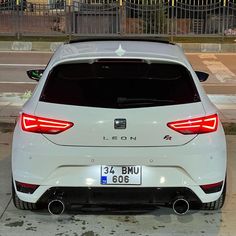 the rear end of a white car parked in front of a fenced off area