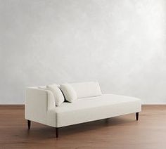 a white couch sitting on top of a hard wood floor next to a wall and window