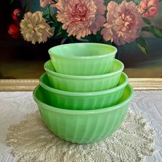 three green bowls are stacked on top of each other in front of a floral painting