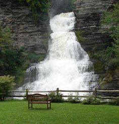 a park bench sitting in front of a waterfall with water falling down it's side