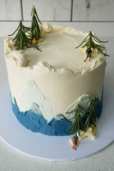 there is a cake with frosting and pine trees on the top, sitting on a plate