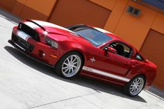 a red and white mustang parked in front of a building