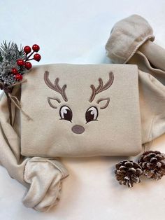 a white bag with reindeer's face on it next to pine cones and red berries