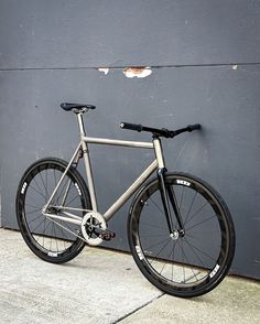 a bike leaning against a gray wall on the sidewalk with no wheels or spokes