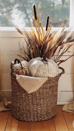 a wicker basket filled with pumpkins and dry grass in front of a window