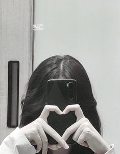 a woman taking a selfie with her cell phone in front of her heart shape