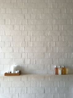 a white brick wall with two candles on the shelf and one candle holder in front of it