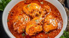 a white bowl filled with meat covered in sauce and garnished with parsley